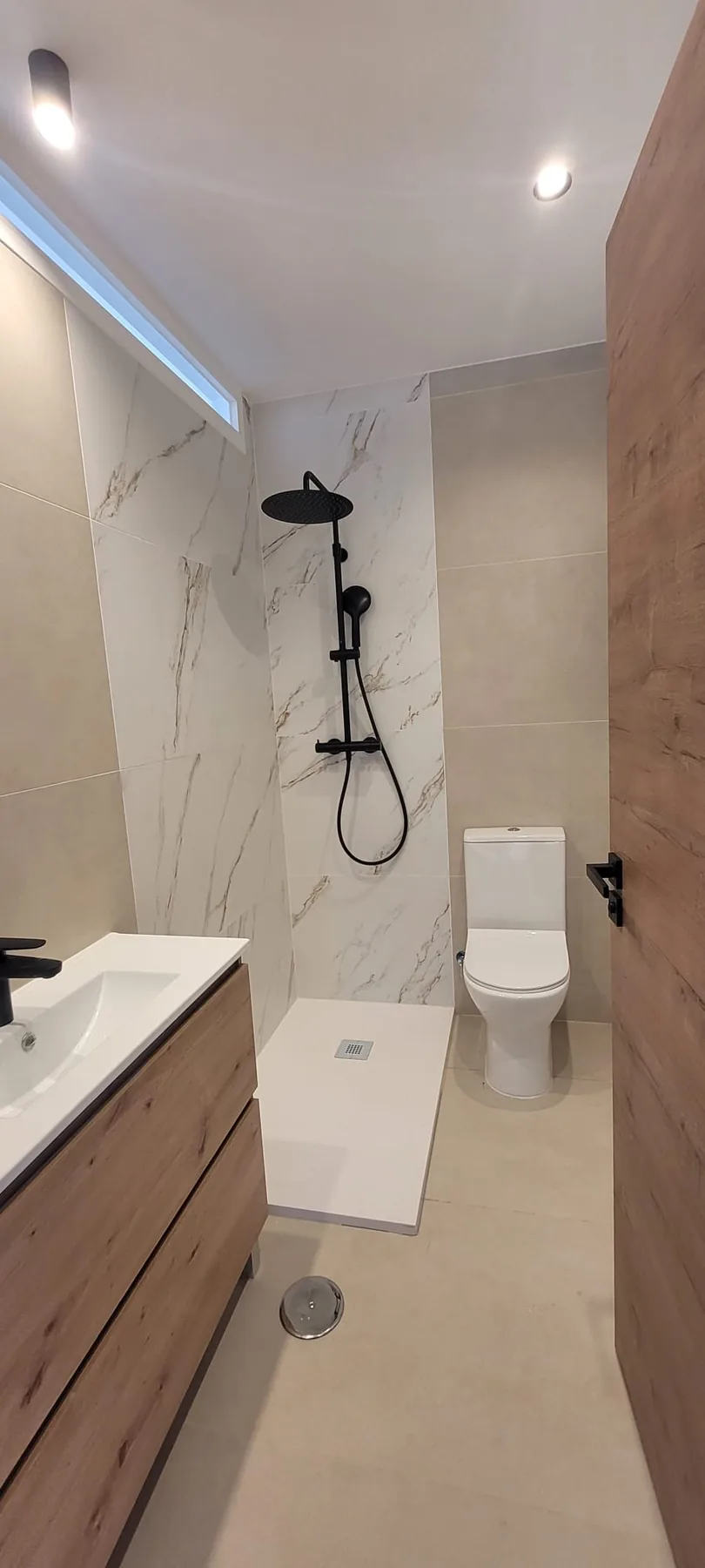 Baño reformado con ducha a ras de suelo y acabados de madera