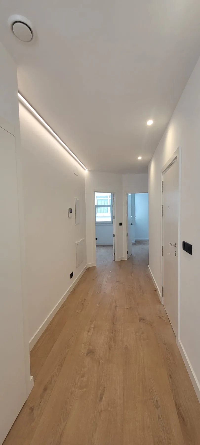 Pasillo renovado con suelo de madera clara e iluminación empotrada